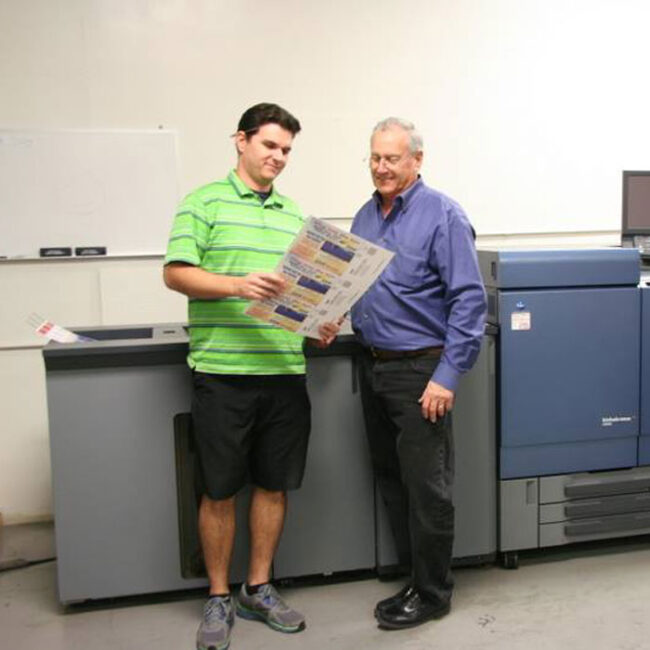 Troy and Loren Ford standing in front of a printing machine